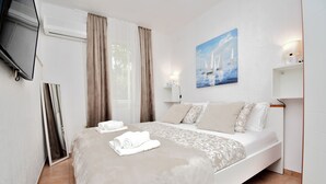 A modern bedroom with a bed, a flat-screen TV mounted on the wall, a painting of sailboats, and a bedside lamp. - House Velebit by the sea (Senj)