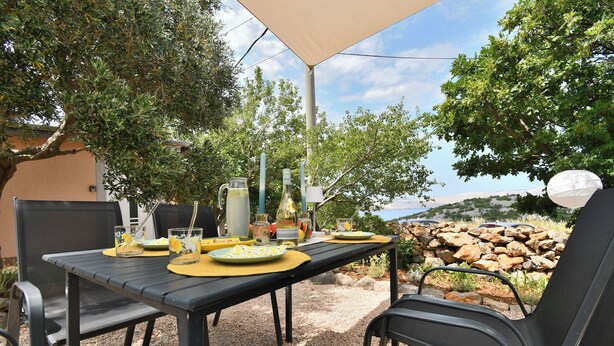 An outdoor dining area with a table set for two, surrounded by chairs, under a canopy. - House Velebit by the sea (Senj)