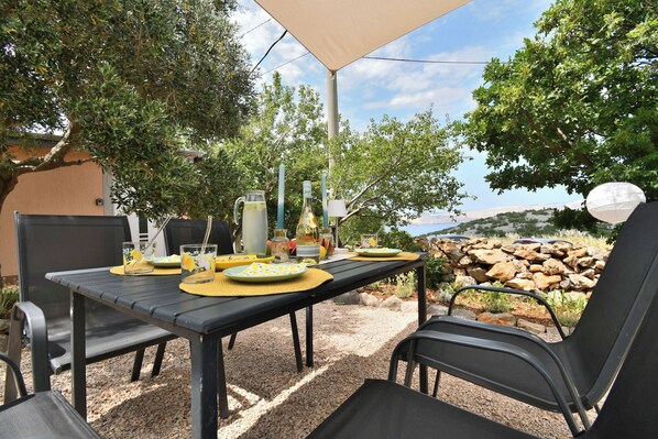 An outdoor dining area with a table set for two, surrounded by chairs, under a canopy. - House Velebit by the sea (Senj)