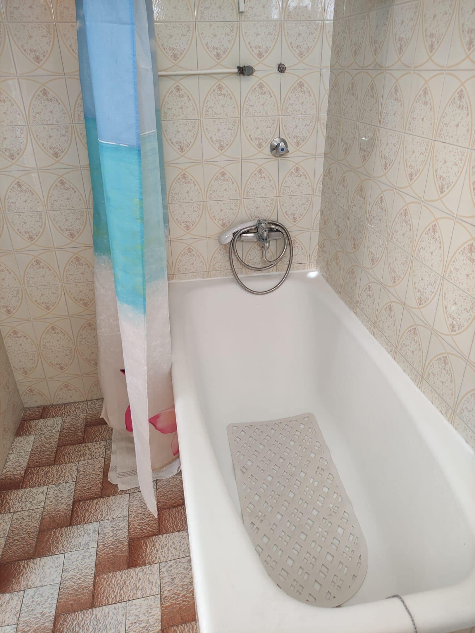 A bathroom with a white bathtub, a shower curtain, and patterned tiles on the walls.