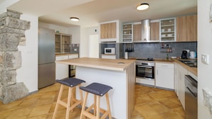 A modern kitchen with a central island, bar stools, a stone accent wall, and built-in appliances. - House Maja (Krk)