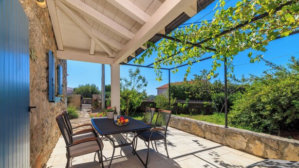 An outdoor patio with a table and chairs, a stone wall, and a pergola with climbing plants. - House Maja (Krk)