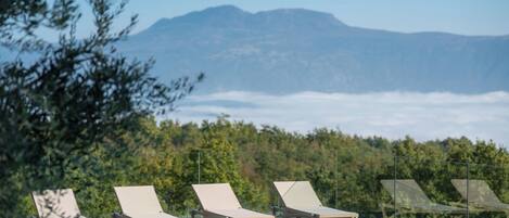 A poolside area with lounge chairs and a view of mountains and forest.