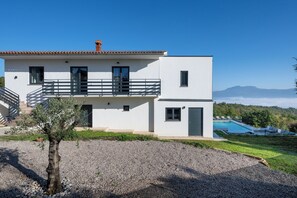 Una casa moderna de dos pisos con balcón, piscina y vistas a las montañas.