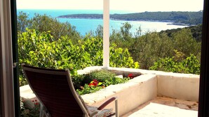 Ein Balkon mit einem Stuhl, Blick auf das Meer und umliegendes Grün.