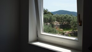 Ein Zimmer mit einem Fenster, das einen Blick auf eine Berglandschaft mit Bäumen und einer Steinmauer bietet.