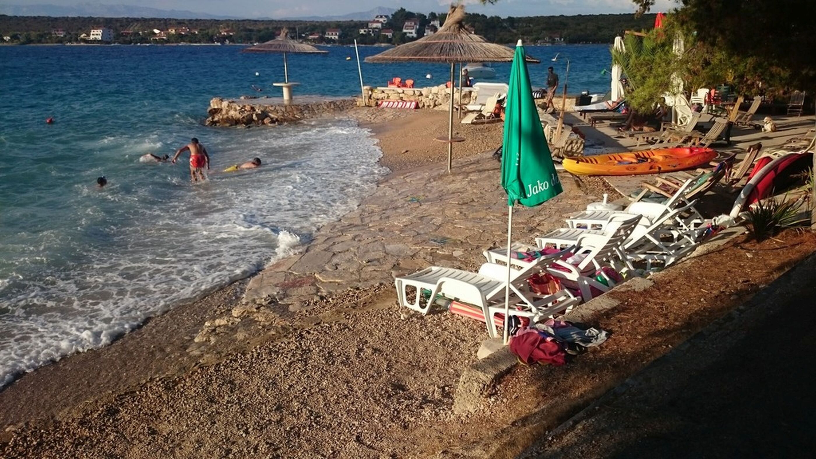 A beach with a rocky shoreline, a few people swimming, and beach chairs and umbrellas.