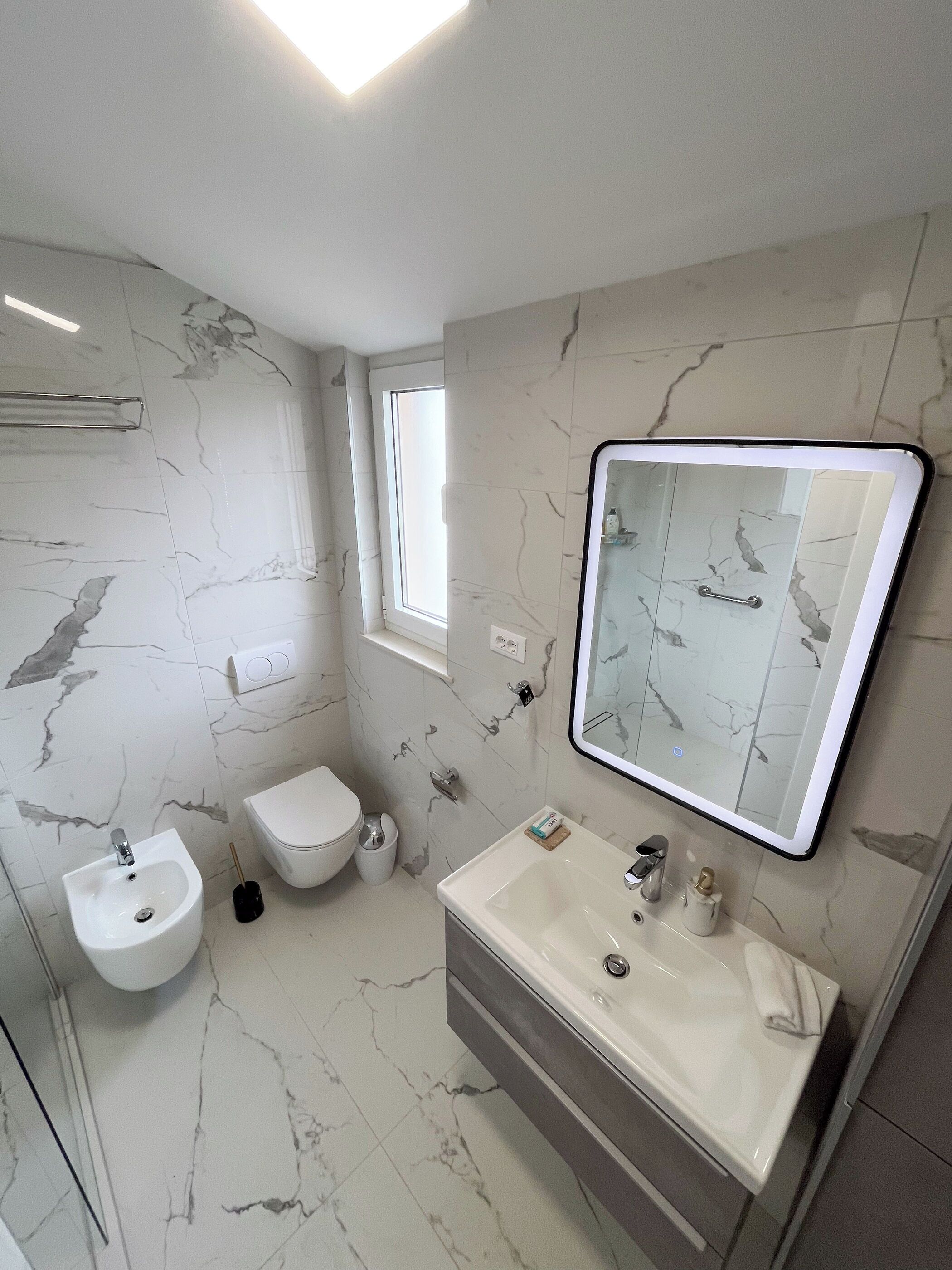 Une salle de bain moderne avec un sol en marbre, un grand miroir, un lavabo et des toilettes.