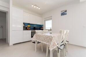A modern kitchen with white cabinets, a blue backsplash, and a dining area with a table and chairs. - Apartment Sankovic (Rovinj)