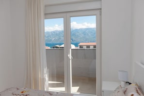 Quarto com vista para montanhas e mar através de uma porta deslizante.