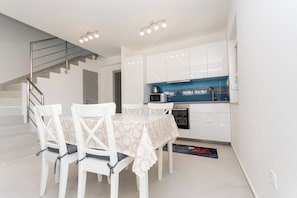 Uma cozinha moderna com armários brancos, painel de parede azul e uma área de refeições com mesa e cadeiras.