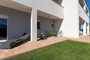 Ein modernes Gebäude mit überdachter Terrasse, Liegestuhl und kleinem Garten.