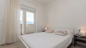 A bedroom with a bed, two bedside tables, a window with curtains, and a view of the outdoors. - Apartment Sankovic (Rovinj)