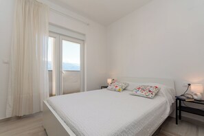 Ein Schlafzimmer mit einem Bett, zwei Nachttischen, einem Fenster mit Vorhängen und Blick ins Freie.