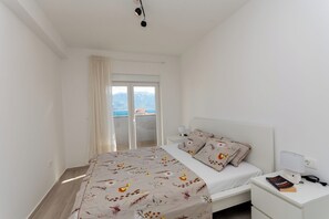 A bedroom with a bed, a bedside table with a lamp, a book, and a view of the sea through a sliding door. - Apartment Sankovic (Rovinj)