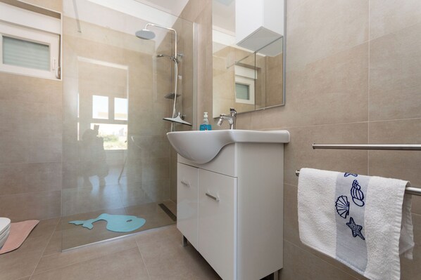 Un baño moderno con ducha de vidrio, lavamanos blanco y una toalla con diseño de caracola.