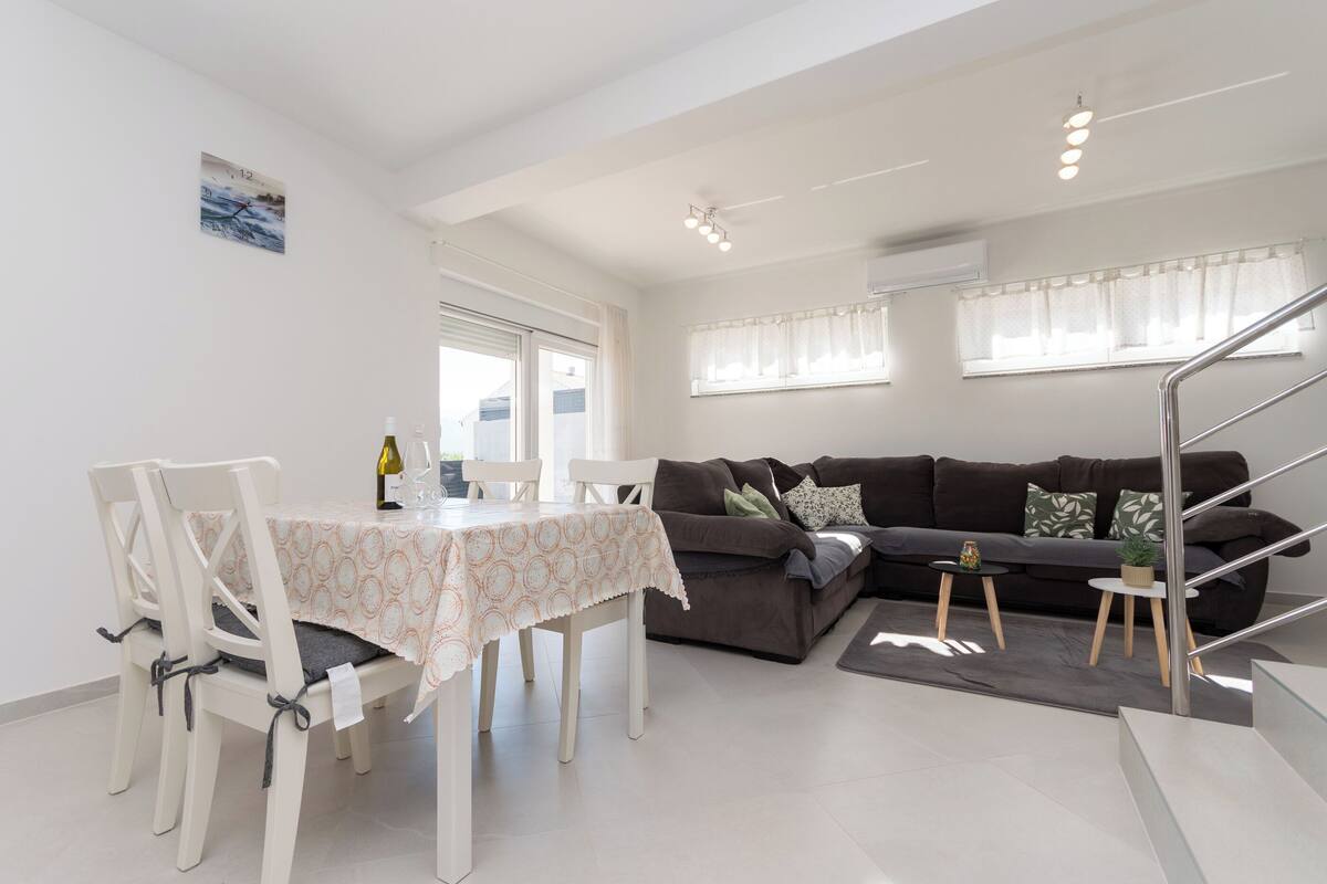 A modern living area with a dining table, chairs, a sofa, and a staircase.