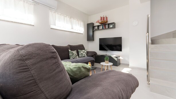 A modern living room with a sofa, a flat-screen TV, a small table with a plant, and a staircase. - Apartment Sankovic (Rovinj)