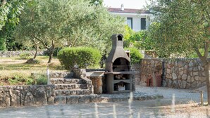 A stone-built outdoor oven in a garden with a stone wall and steps leading up to it. - Apartments Kamenar (Dobrinj)