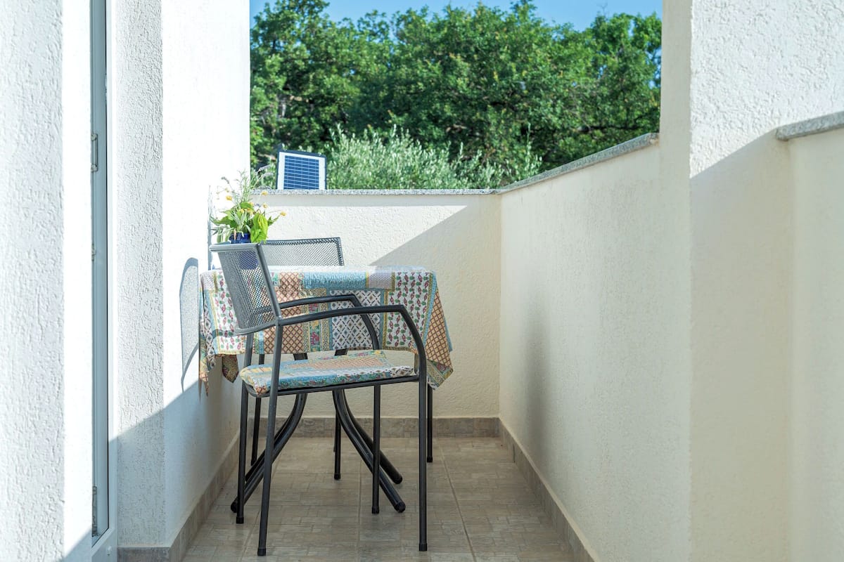 A small outdoor patio area with a table and two chairs, a potted plant, and a solar panel.