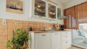 A kitchen with white cabinets, a potted plant, and a window with blinds. - Apartments Kamenar (Dobrinj)