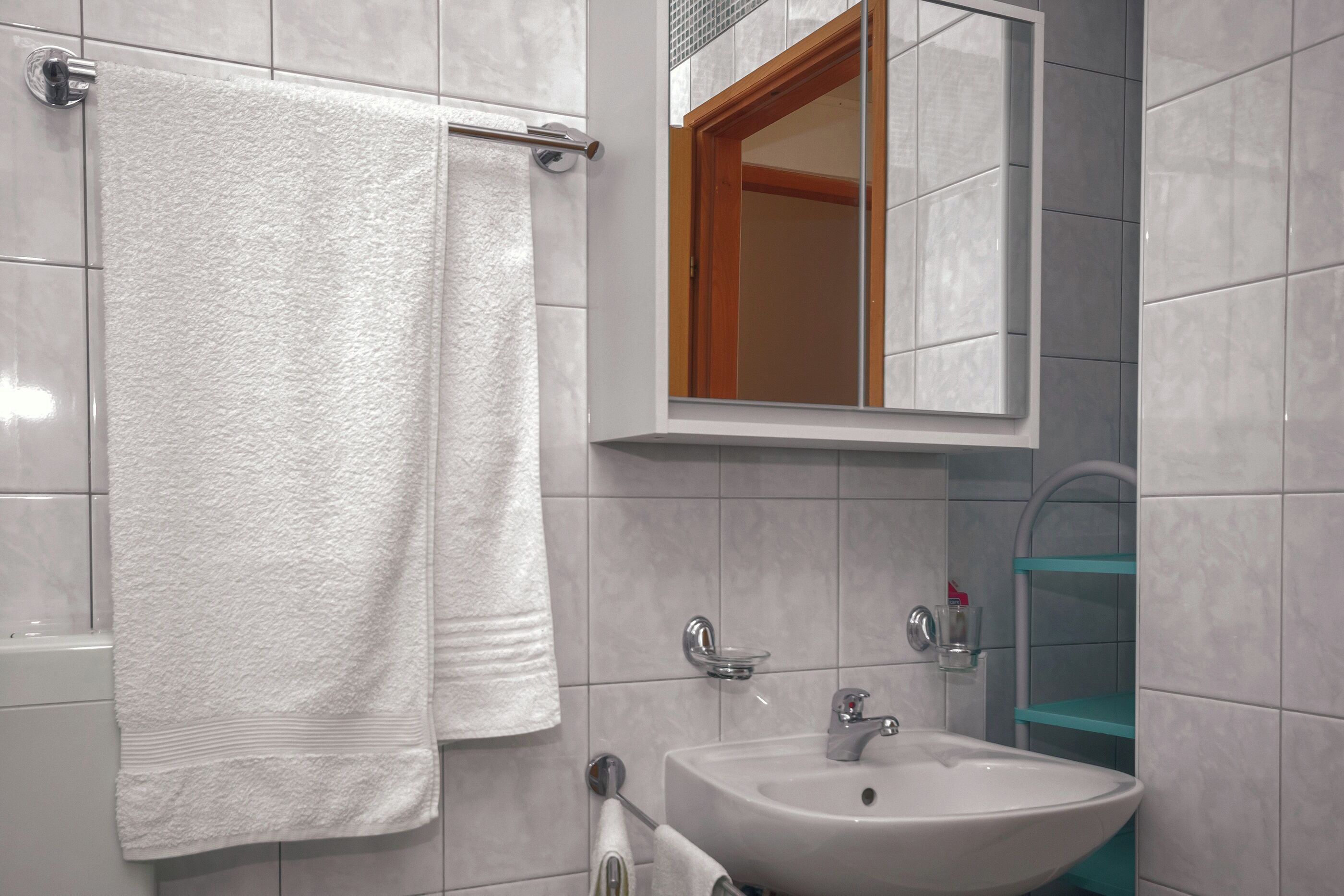 Een badkamer met een witte wastafel, een spiegel en een handdoekrek.