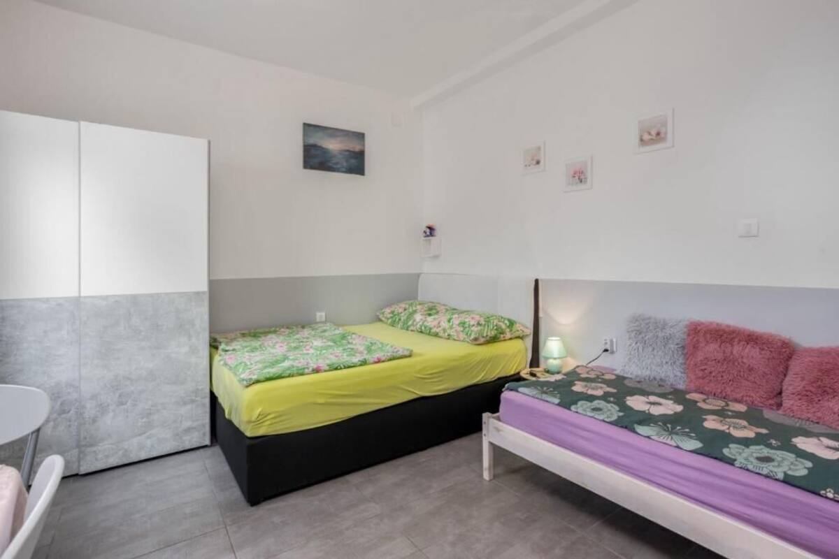A small, well-lit bedroom with two beds, a wardrobe, and a small table.