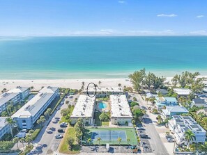 Luftaufnahme eines Küstenhotels mit Pool, Tennisplatz und direktem Zugang zum Strand.
