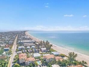 Luftaufnahme eines Küstenwohngebiets mit Strandhäusern, blauem Himmel und einer gut sichtbaren Straße.