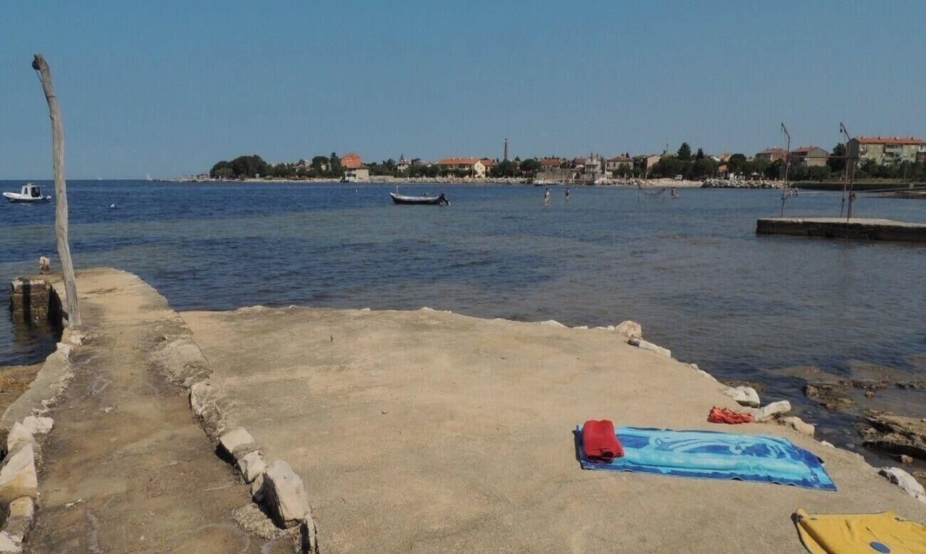Een kustgezicht met een betonnen pier, boten en een verre kustlijn met gebouwen.