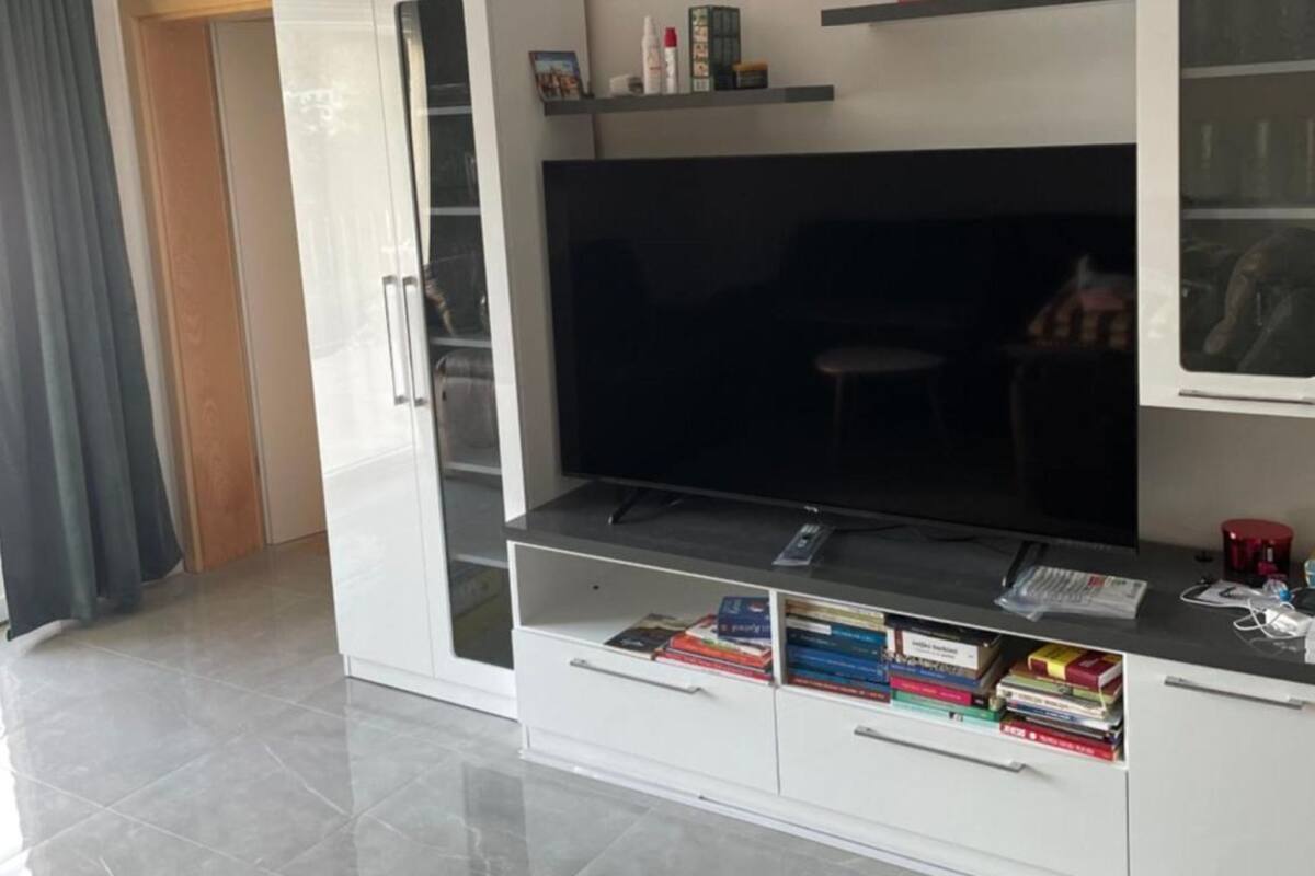 A modern living room with a large flat-screen TV, built-in shelving with decorative items, and a glass-front cabinet.