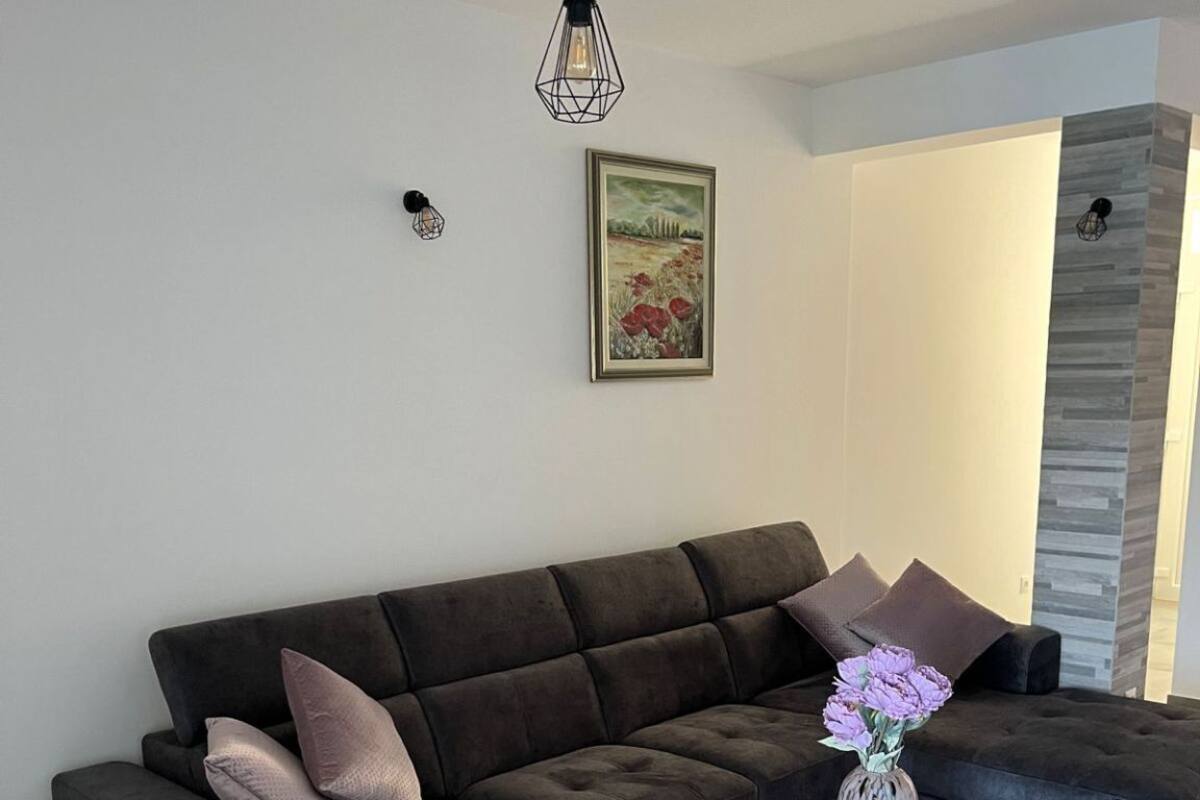A modern living room with a dark brown sofa, a small round table with a vase of flowers, and a framed picture on the wall.