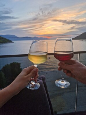 Two people holding wine glasses on a balcony overlooking a body of water with a sunset in the background. - Apartments Damir (Slivno)