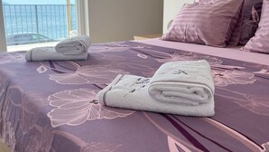 Ein ordentlich bezogenes Bett mit einem blumigem Bettüberwurf, ein gefaltetes weißes Handtuch und mehrere Kissen.