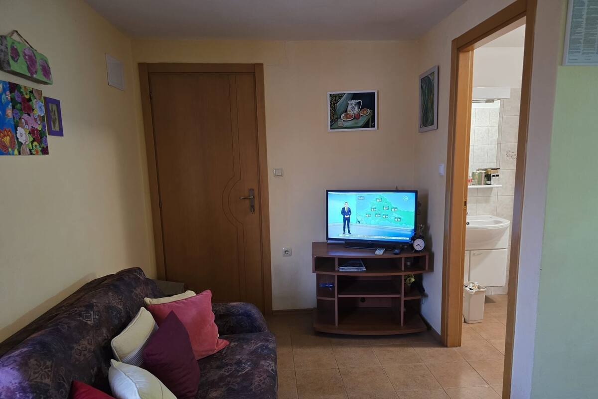 A living room with a sofa, television, and a door leading to a bathroom.