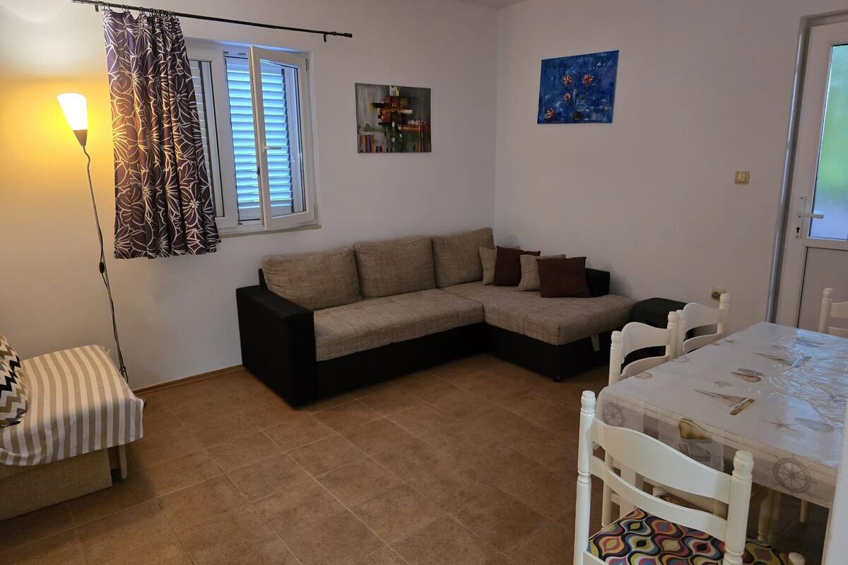 A living room with a sofa, a dining table with chairs, a lamp, and a window with blinds.