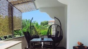 A small, enclosed outdoor patio with a table and chairs, a hanging chair, and a view of greenery and buildings in the background. - House Solis (Rab)