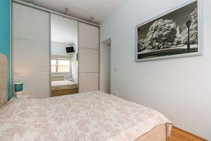 A bedroom with a bed, a bedside table, a lamp, a window, a sliding door, and a framed picture on the wall. - Apartment Mandria (Opatija)