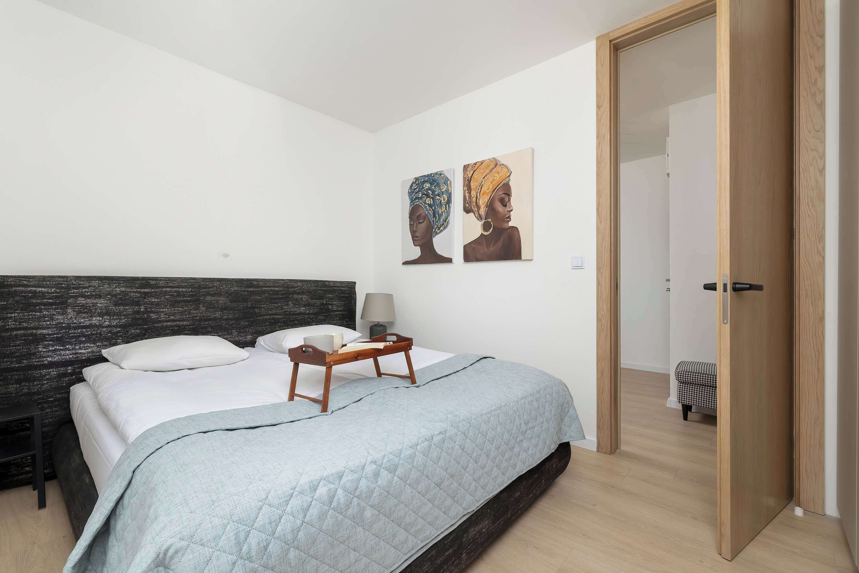 Un dormitorio con una cama, una mesita de noche, dos obras de arte colgadas en la pared y una puerta de madera.