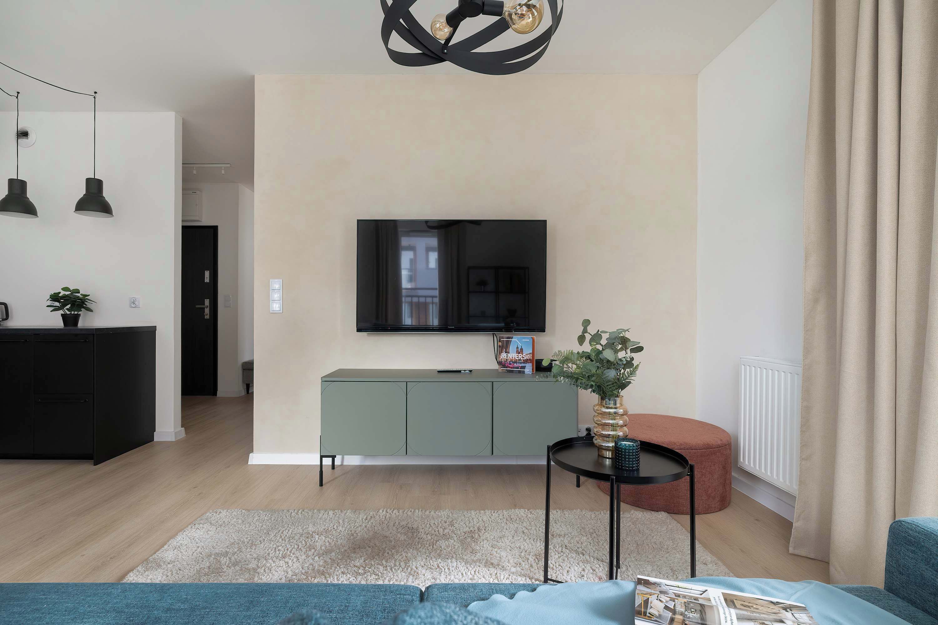 A modern living room with a flat-screen TV mounted on the wall, a green cabinet, a round ottoman, and a blue sofa.