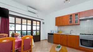 A modern kitchen with wooden cabinets, a dining area with a table and chairs, and a view through large windows. - Apartment Damjan (Kastelir-Labinci)