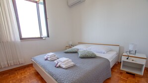 A neatly made bed with pillows, a bedside table with a lamp, and a window with curtains. - Apartments Dalmatino (Biograd na Moru)