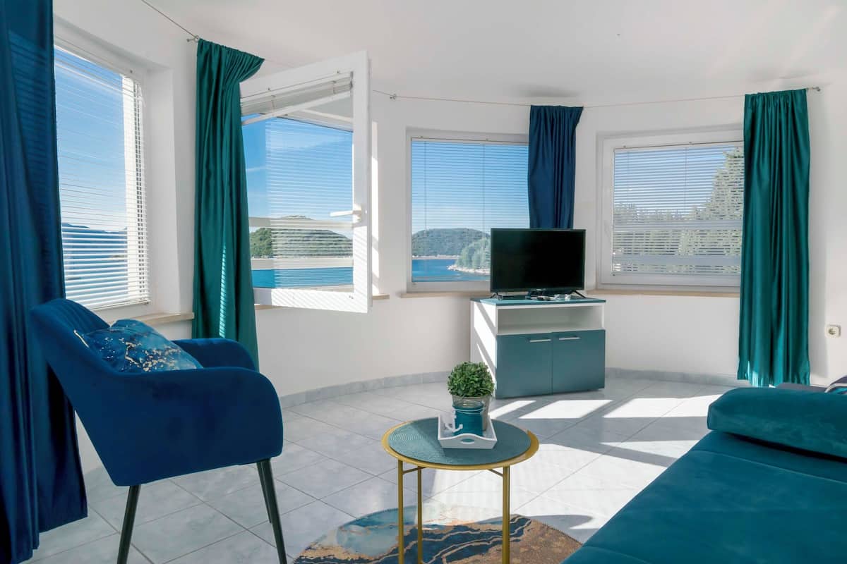 A modern living room with a sofa, a chair, a TV, and a view of the sea.