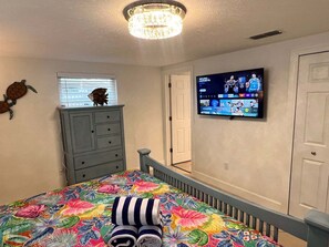 Ein Schlafzimmer mit einem Bett, einem Schminktisch, einem Fernseher und einer Deckenleuchte.