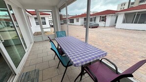 Ein überdachter Patio-Bereich mit Tisch und Stühlen, einer Fußmatte und Blick auf die umliegenden Gebäude.