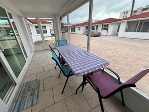 Ein überdachter Patio-Bereich mit Tisch und Stühlen, einer Fußmatte und Blick auf die umliegenden Gebäude.
