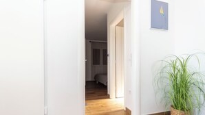 Ein Korridor mit Holzboden, weißen Wänden und einer Topfpflanze.