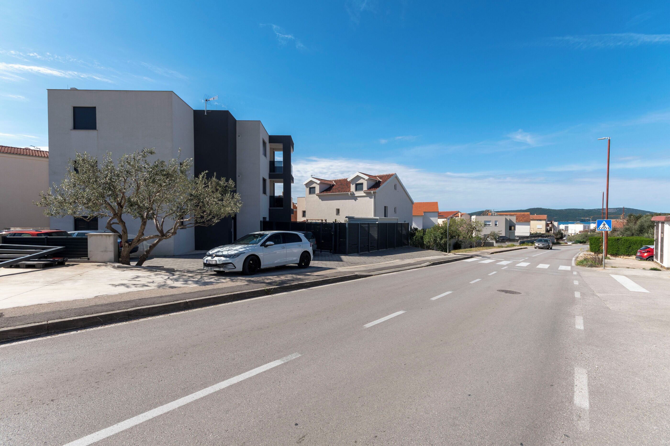 Eine Straße mit modernen Gebäuden, ein weißes Auto, das am Straßenrand geparkt ist, und ein klarer, blauer Himmel.