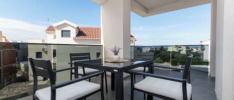 A balcony with a glass table and chairs, a potted plant, and a view of neighboring houses.