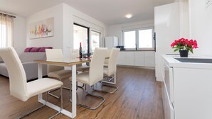 Eine moderne Küche mit weißen Schränken, ein Essbereich mit Glastisch und ein Wohnzimmer mit Sofa und Gemälde.